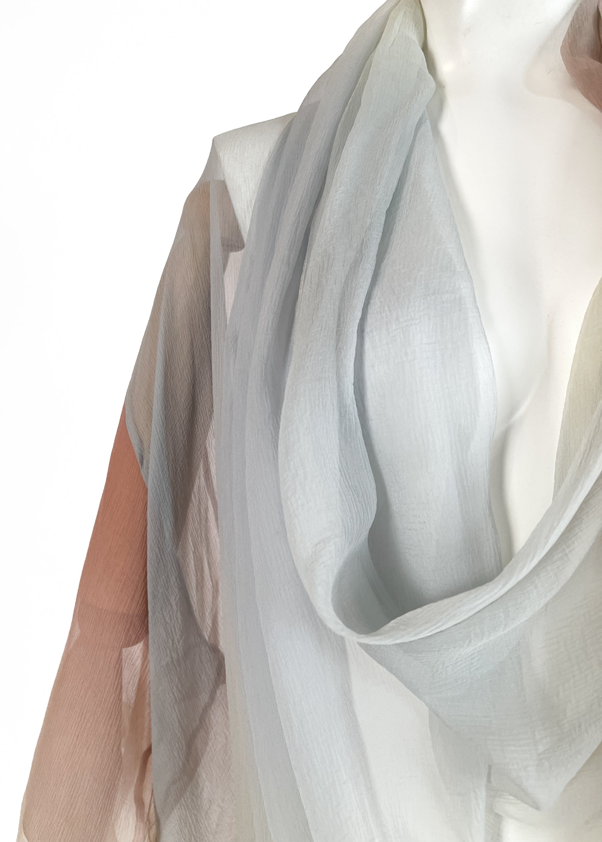 Detail on neckline from a 1989 Romeo Gigli sheer silk kimono-style wrap top draped on a mannequin. Features a soft pastel gradient transitioning from pale blue and grey to rose pink and ivory, with a draped cowl neckline and wide, fluid sleeves.